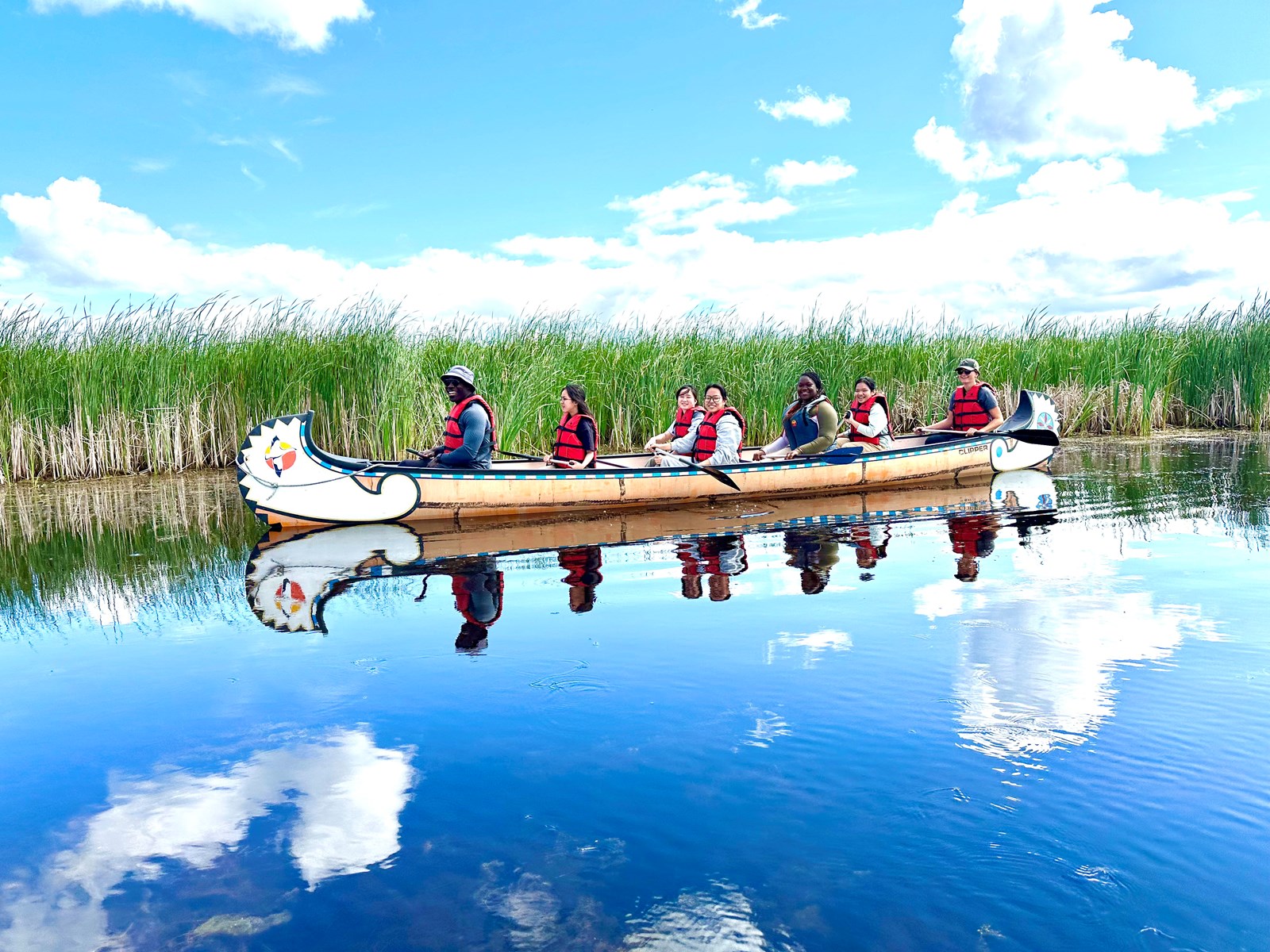 Seven International Summer Program participants sit in a long canoe at Oak Hammock Marsh.