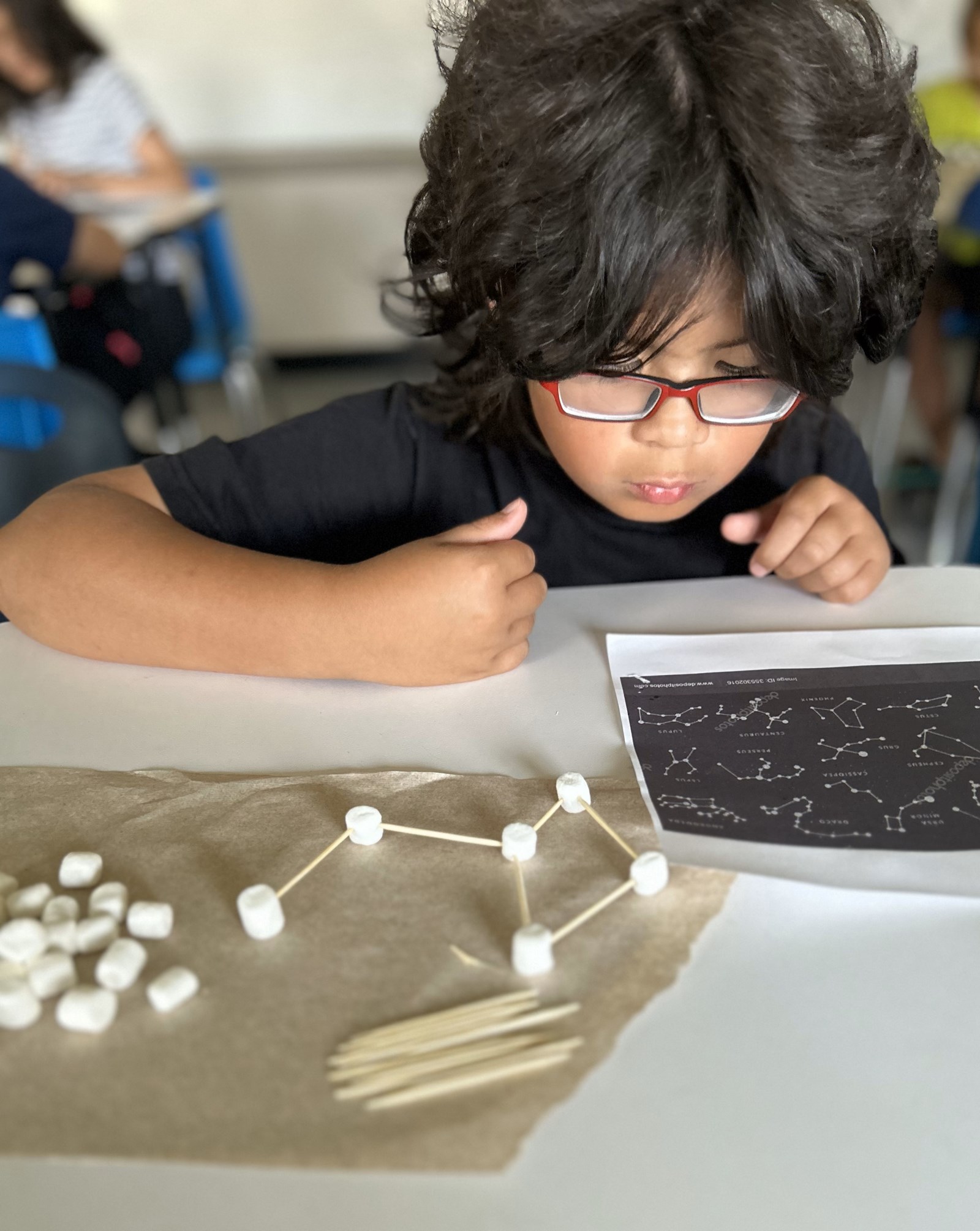 A child crafts an astrological constellation using marshmallows and toothpicks.