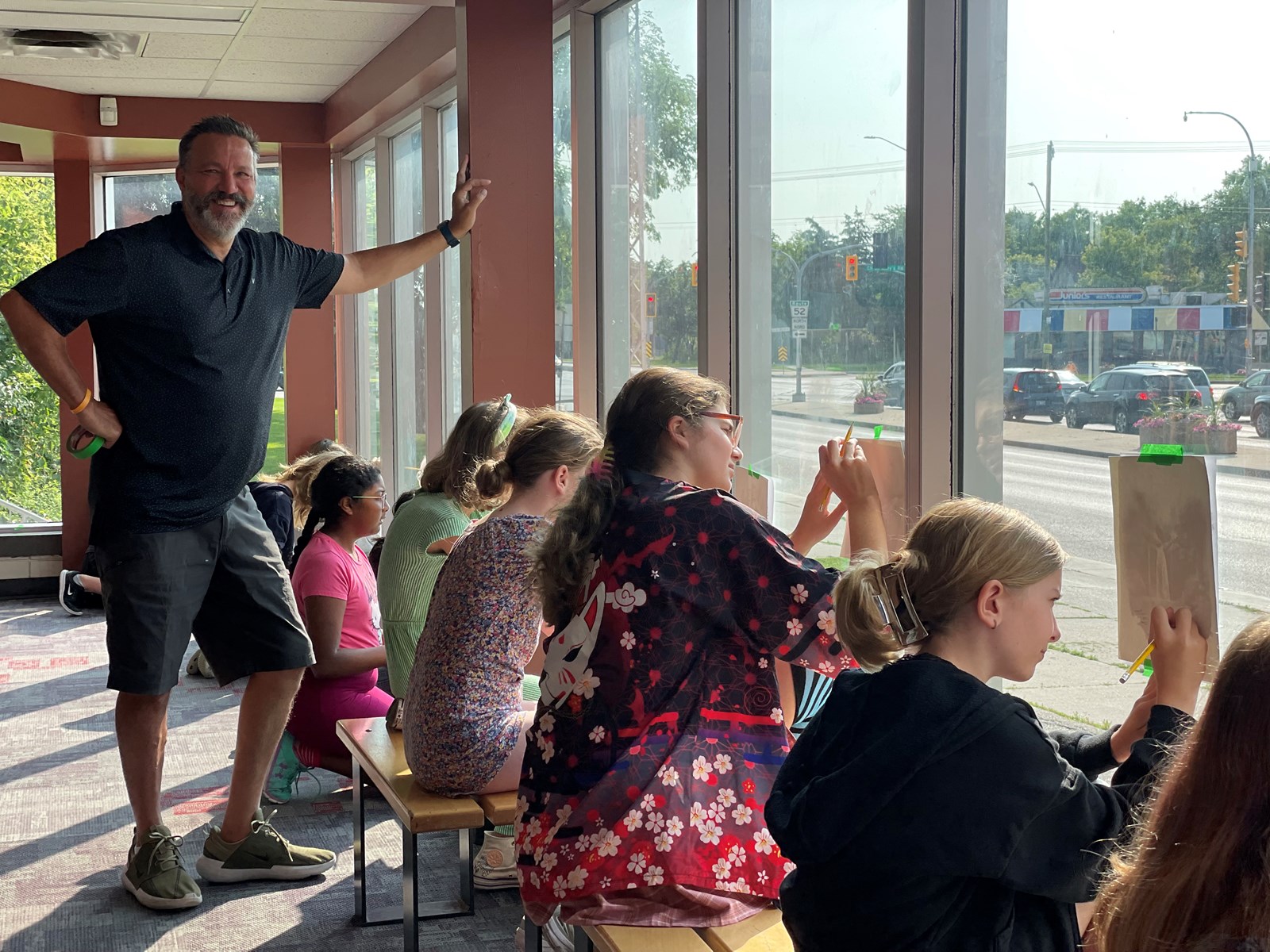 Summer art camp participants trace images on paper that is taped to a window.