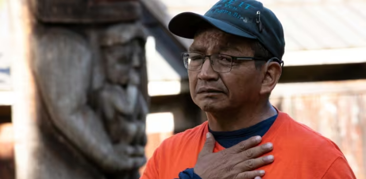 Indigenous man in an orange t-shirt with hand over heart
