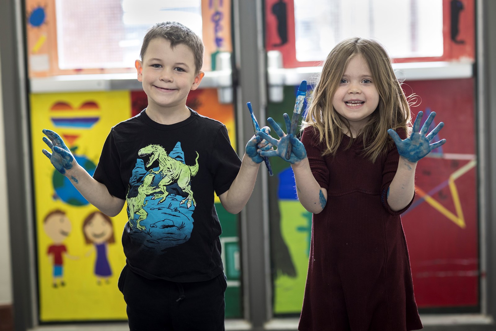 Two students with their hands painted blue holding paint brushes in front of an entry way