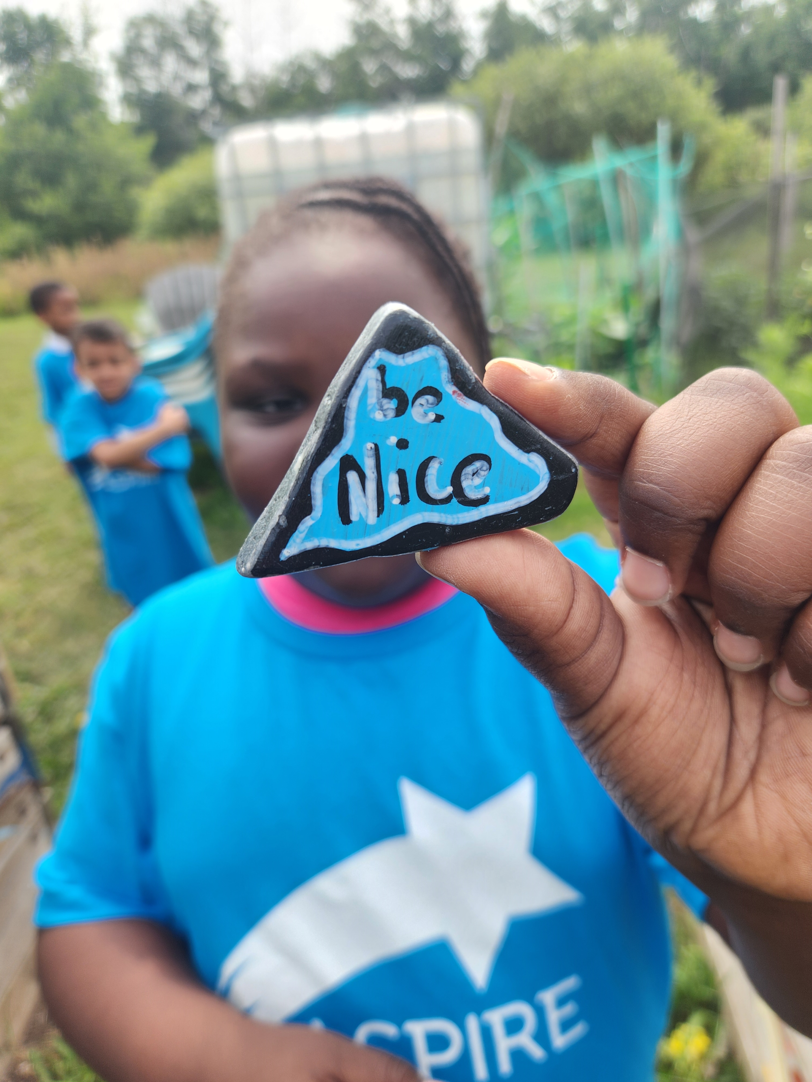 Student holding up a painted rock that says: Be Nice