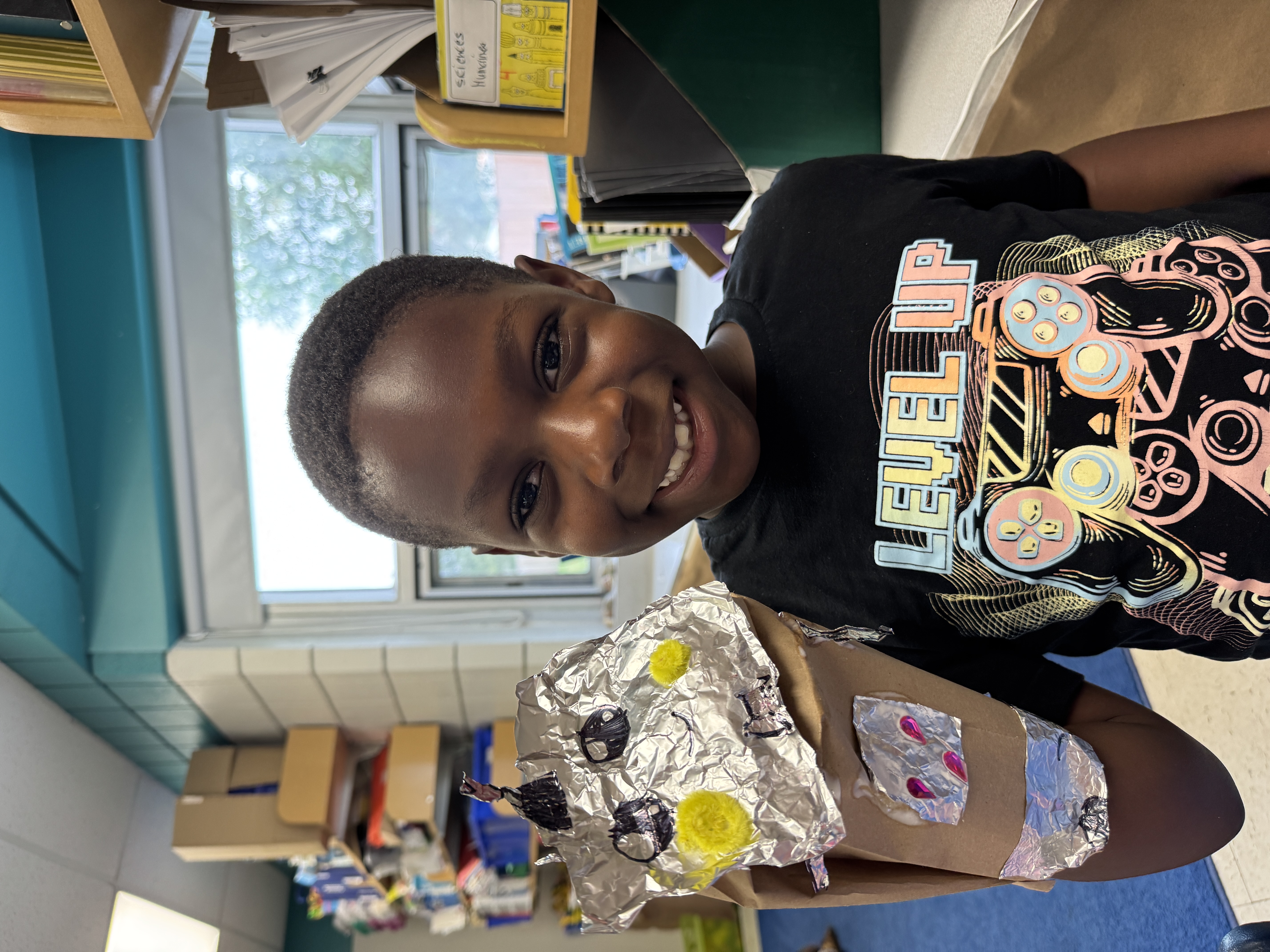 Student showing off a craft made out of aluminum and cardboard